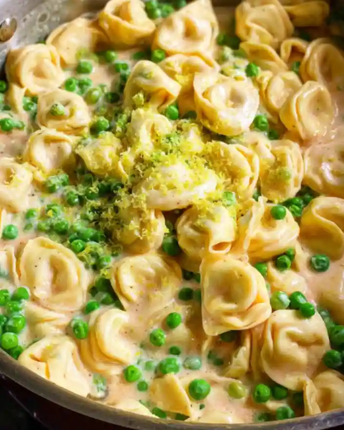 Creamy tortellini with peas and fresh lemon zest simmering in a skillet