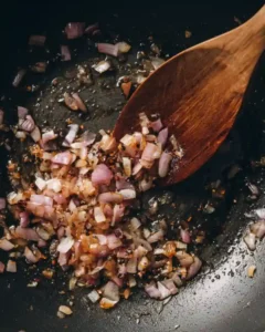 Finely chopped shallots sautéing in a skillet with a wooden spoon