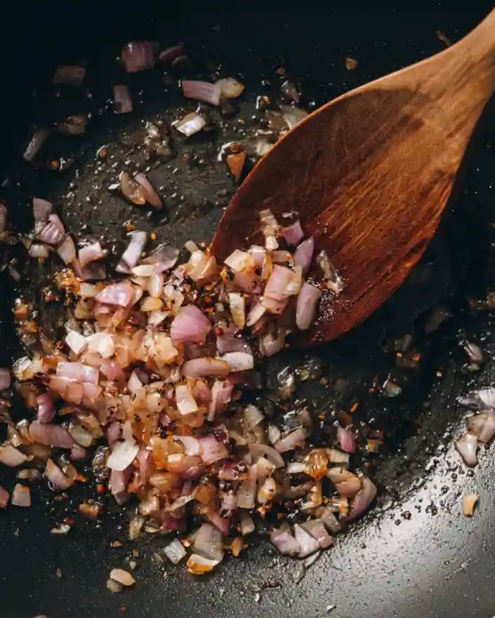 Finely chopped shallots sautéing in a skillet with a wooden spoon