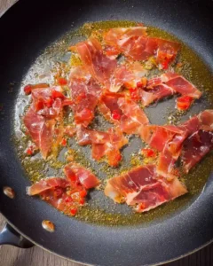 Slices of prosciutto crisping in butter in a black nonstick skillet