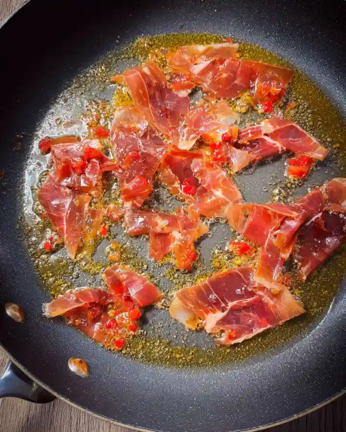 Slices of prosciutto crisping in butter in a black nonstick skillet