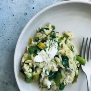 A plated bowl of creamy one-pot orzo risotto spring veggies, garnished with fresh dill.
