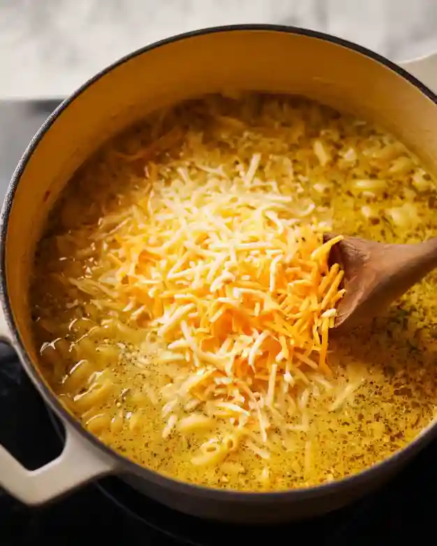 Stirring cheese and cream into macaroni cheeseburger soup
