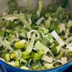 Sautéing chopped leeks in a large pot for one-pot orzo risotto.