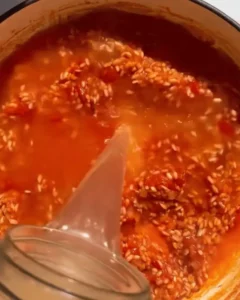 Pouring hot broth into a pan of rice and tomato mixture for One-Pan Salsa Verde Shrimp and Rice.