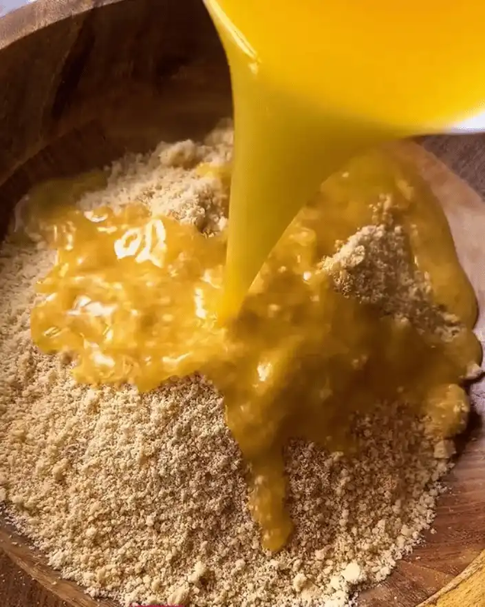 Pouring melted butter into crushed biscuits for cheesecake base