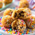 No Bake Moose Farts 1 Close-up of No Bake Moose Farts cookie balls with chocolate chips and coconut, topped with colorful sprinkles on a white plate, one bitten open to show the soft interior.