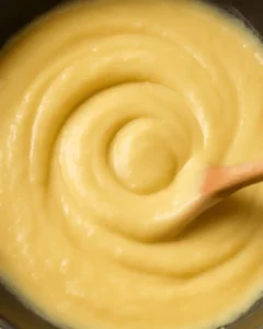 Thick pastry cream custard being stirred in a saucepan with a wooden spoon.