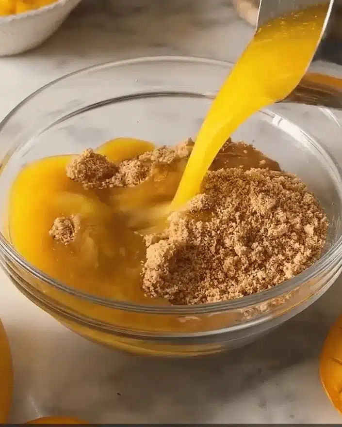 Melted butter being poured from a measuring cup into a glass bowl filled with crushed biscuits for a no bake mango dessert recipe.