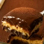 A spoon lifting a slice of no bake Boston cream pie bar showing biscuit, custard, and chocolate ganache layers.