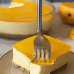A spoon lifting a perfect scoop from a finished no bake mango dessert, clearly showing the jelly, cream, and biscuit layers.