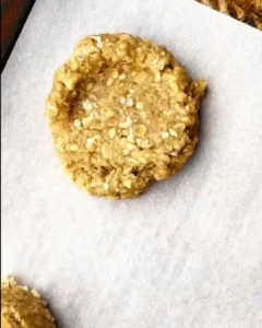 Uncoated lemon no bake oatmeal cookie resting on a baking sheet lined with parchment paper.