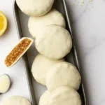 A tray filled with lemon no bake oatmeal cookies coated in white chocolate, with one cookie cut open to reveal its chewy interior.