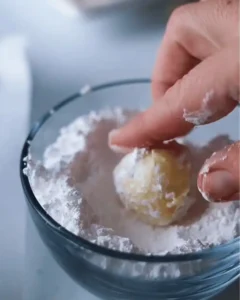 rolling orange creamsicle truffle in powdered sugar coating