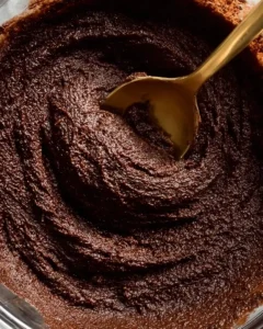 mixing thick fudgy brownie batter base with a gold spoon in a glass bowl