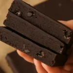 Stack of no bake healthier brownies with glossy chocolate topping held in hand