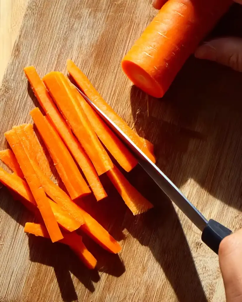 Cutting fresh carrots lengthwise on a wooden board.