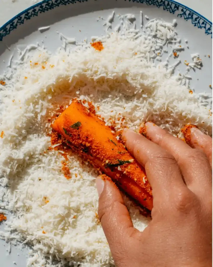 Dipping seasoned carrot in grated parmesan cheese.