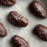 No-Bake Dark Chocolate Stuffed Dates setting on parchment sprinkled with sea salt